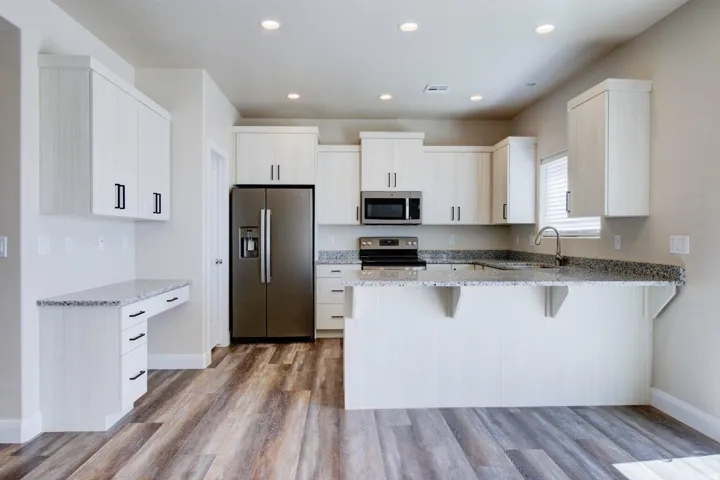 Kitchen featuring stainless steel appliances, a breakfast bar, light stone countertops, a peninsula, and light wood-style floors