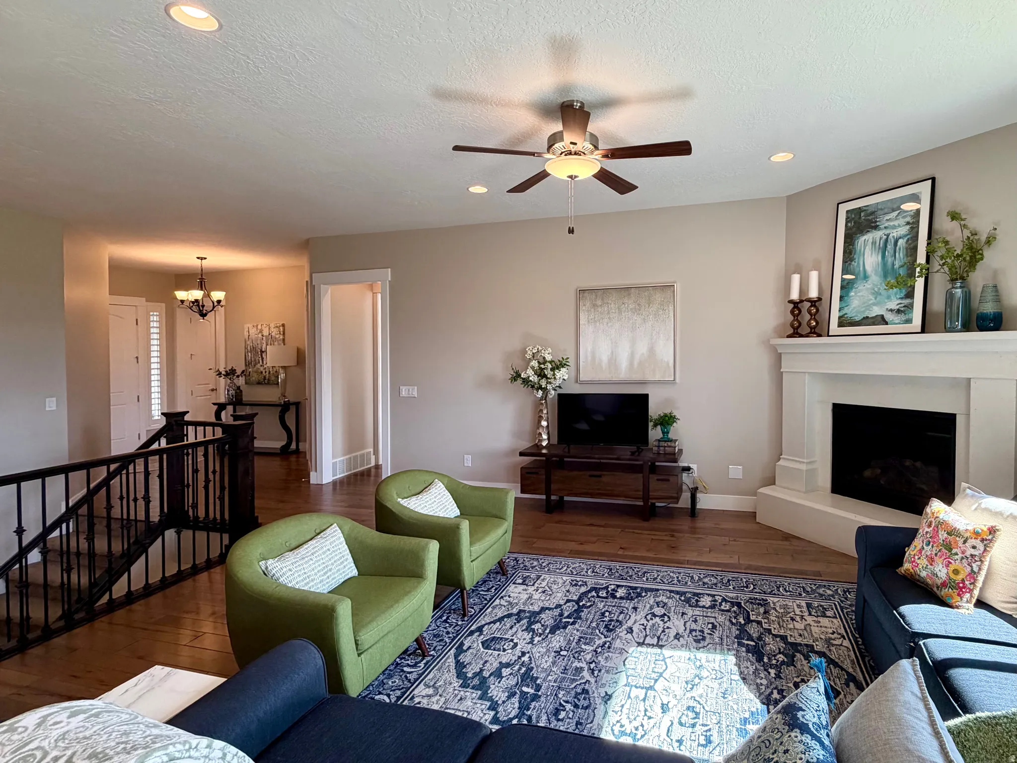 Living room featuring wood finished floors, ceiling fan, suspended lighting, and a fireplace with raised hearth