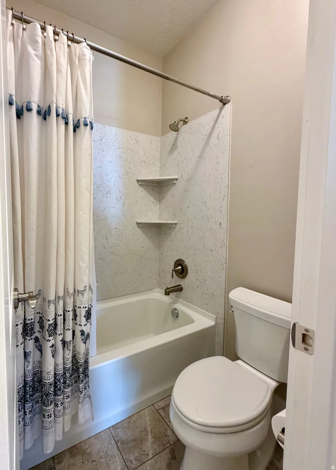 Bathroom with shower / bathtub combination with curtain, a textured ceiling, and tile patterned flooring