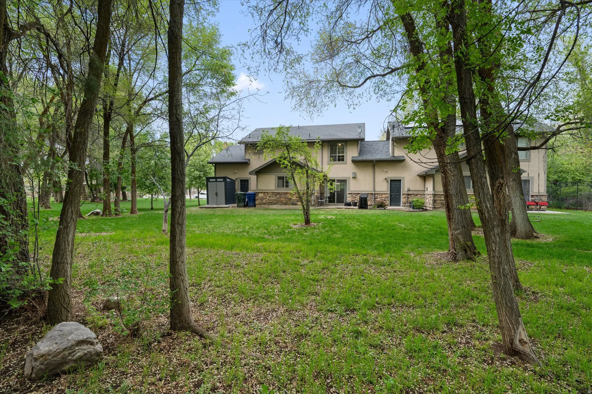 Rear view of house with stucco siding, stone siding, a yard, a storage unit, and a patio