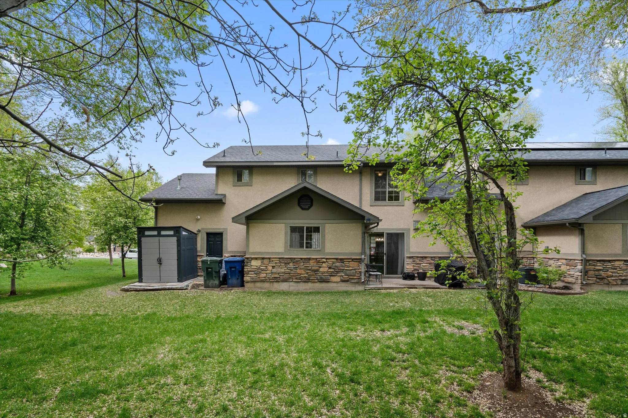 Back of property featuring a storage shed, stucco siding, stone siding, and a lawn