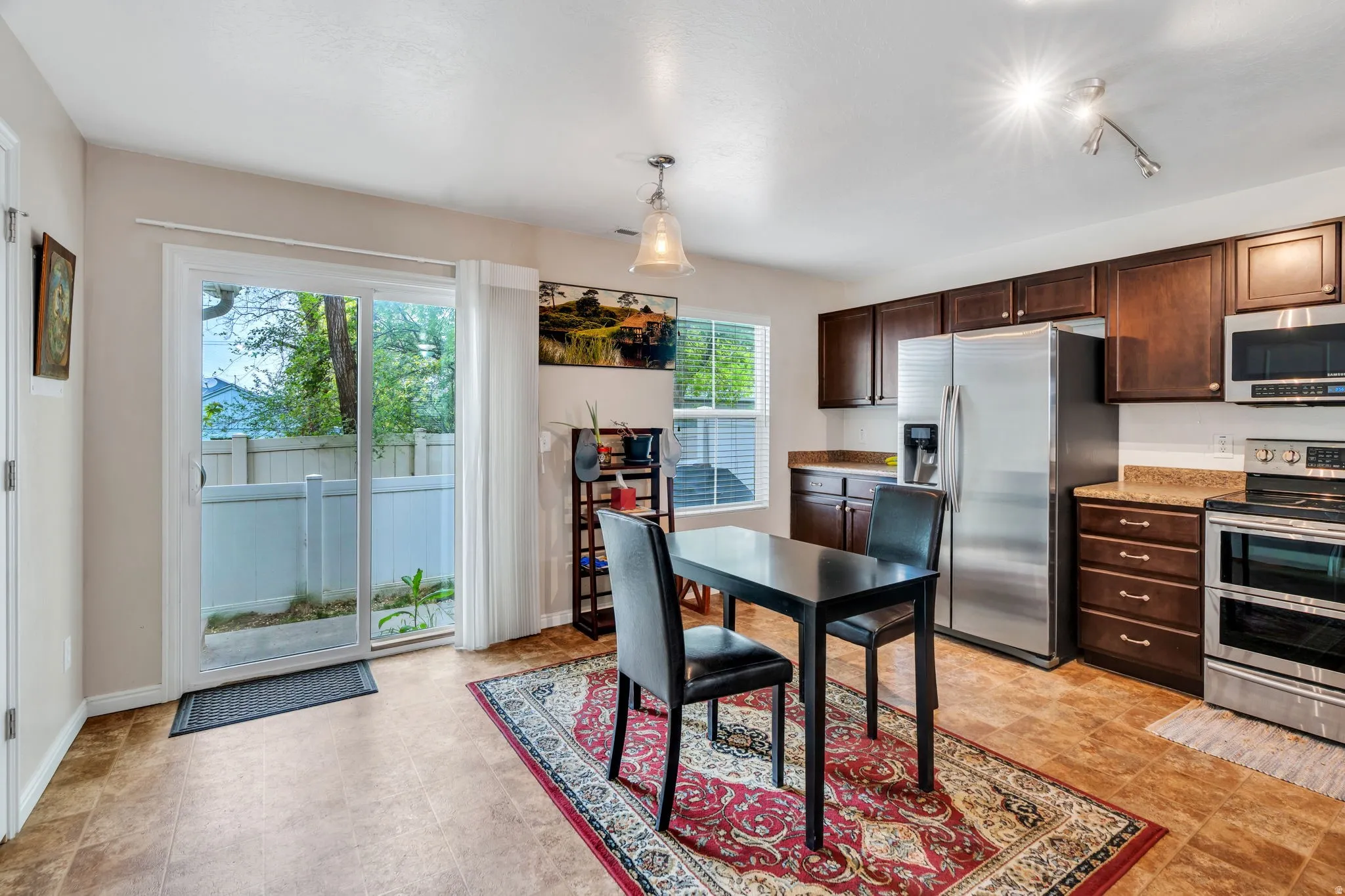 Kitchen with dark wood finish cabinetry, stainless steel appliances, decorative light fixtures, and light stone counters