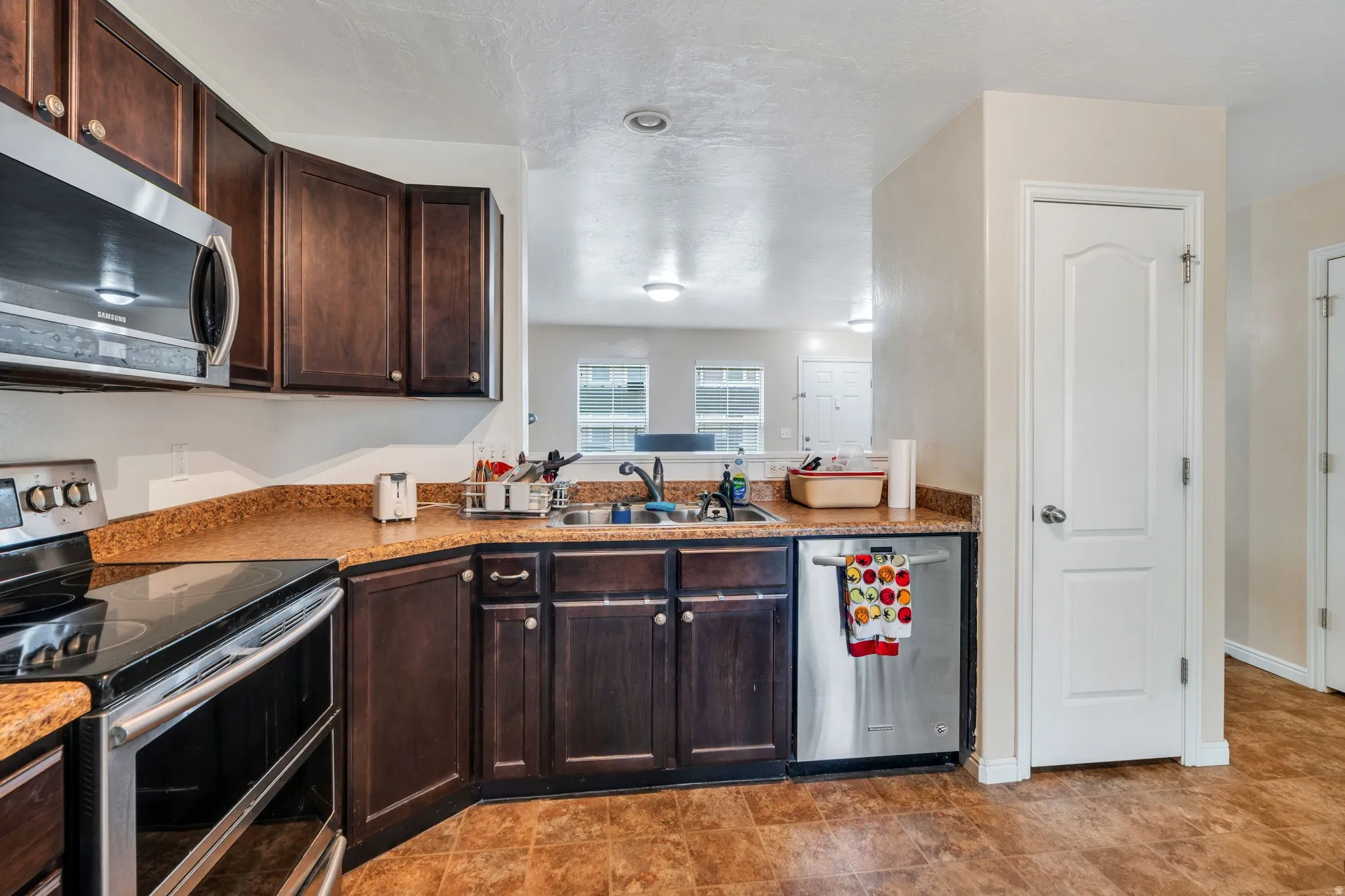 Kitchen featuring stainless steel appliances, dark wood finish cabinets, and light countertops