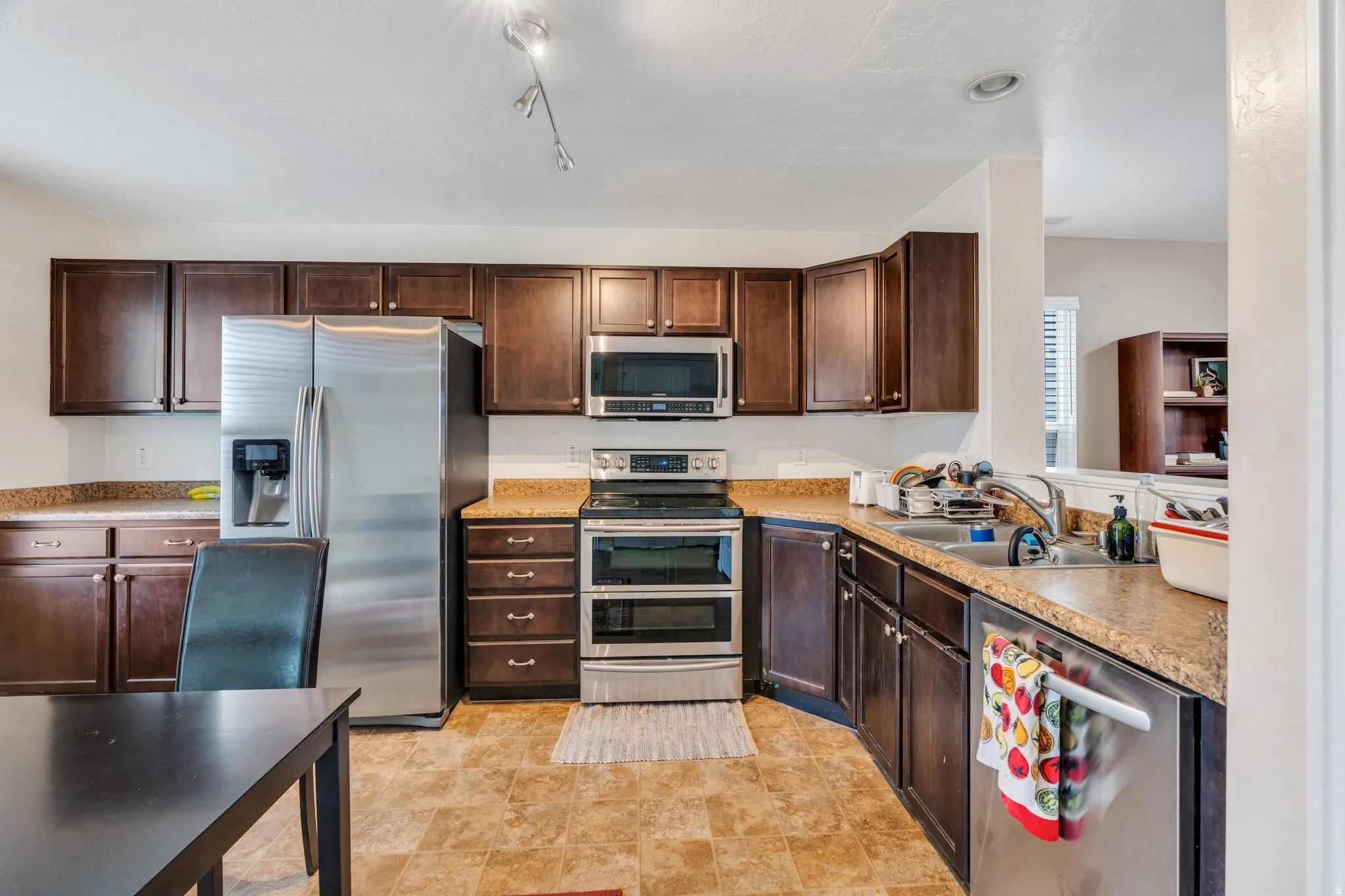 Kitchen with stainless steel appliances, dark wood finish cabinets, light countertops, and stone finish flooring