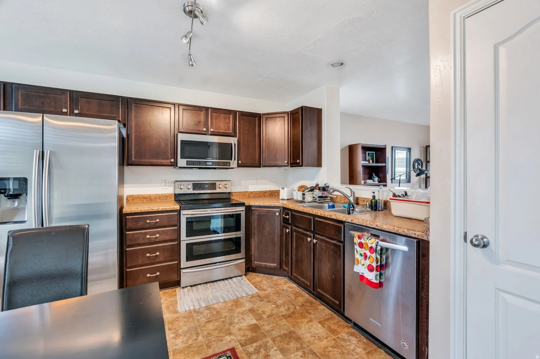 Kitchen with stainless steel appliances, dark wood finish cabinetry, and stone finish floors