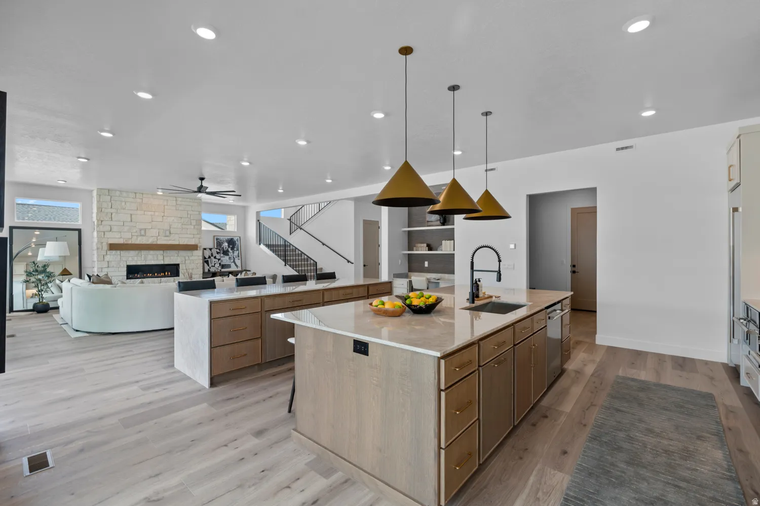 Kitchen with open floor plan, a stone fireplace, light stone countertops, light wood-type flooring, and a ceiling fan