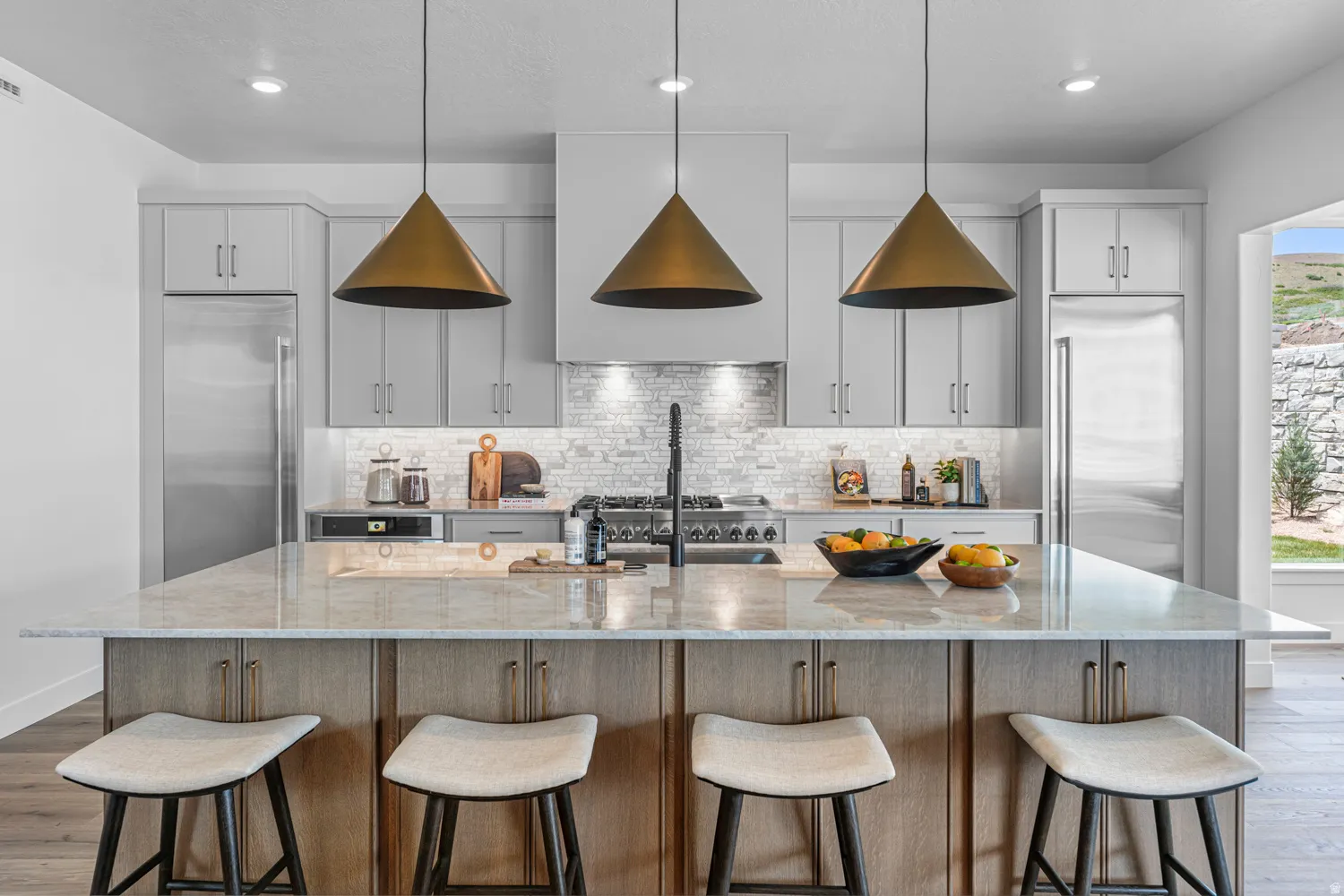 Kitchen with light wood-style flooring, a kitchen bar, a large island with sink, and light stone countertops