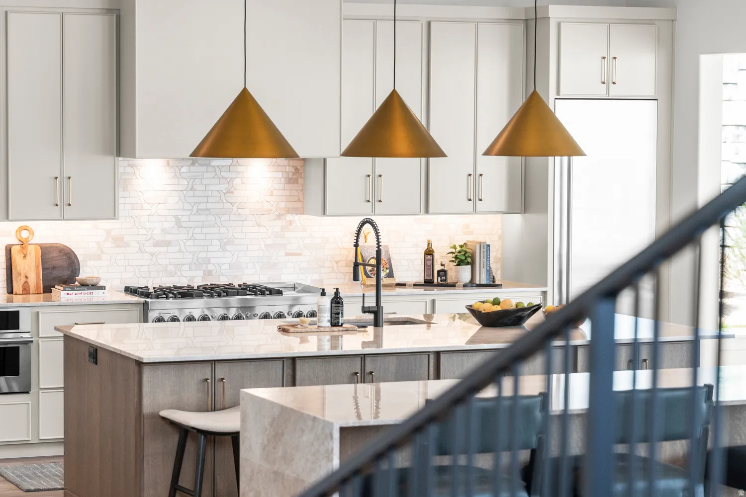 Dual tone kitchen with light stone countertops, a center island with sink, stainless steel oven, a kitchen bar, and backsplash