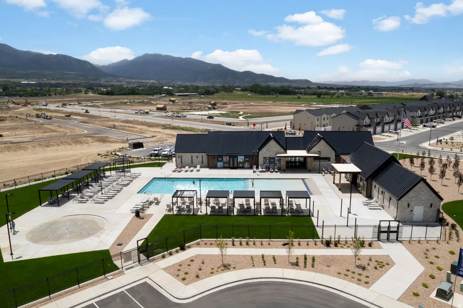 Modern community amenity center featuring a rectangular swimming pool, integrated shallow splash pad, and multiple shaded lounge areas