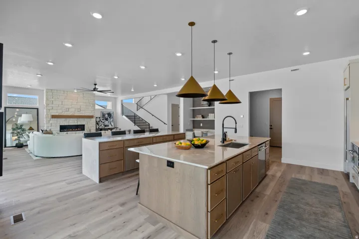 Kitchen with open floor plan, a stone fireplace, light stone countertops, light wood-type flooring, and a ceiling fan