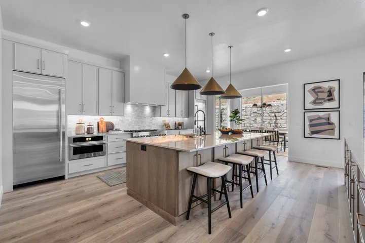 Kitchen featuring light stone countertops, an island with sink, stainless steel appliances, dual tone cabinetry, and light wood-style floors