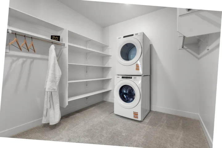 Laundry room featuring stacked washer / dryer and light carpet