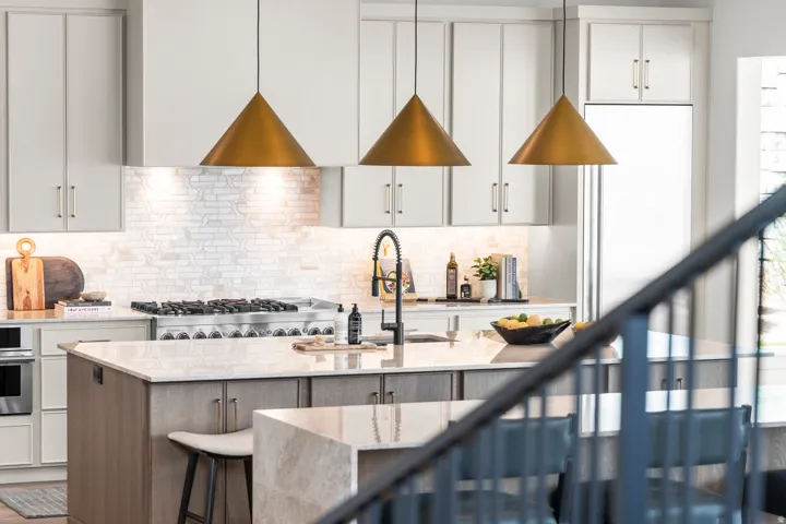 Dual tone kitchen with light stone countertops, a center island with sink, stainless steel oven, a kitchen bar, and backsplash
