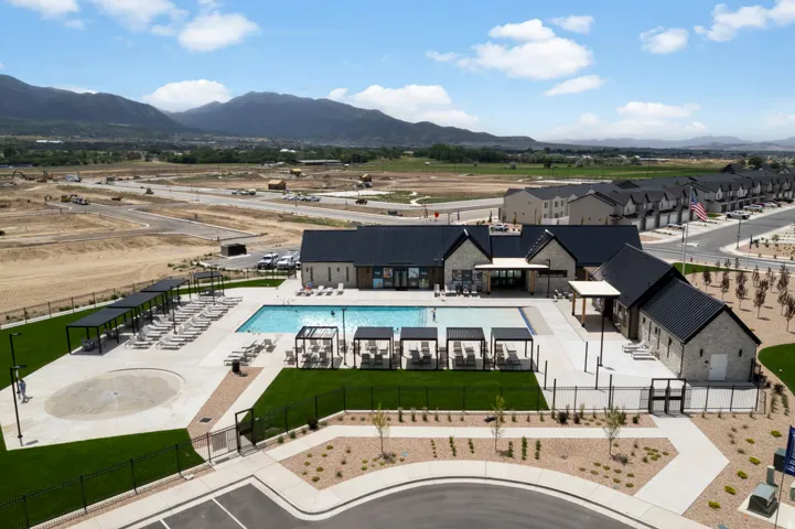 Modern community amenity center featuring a rectangular swimming pool, integrated shallow splash pad, and multiple shaded lounge areas