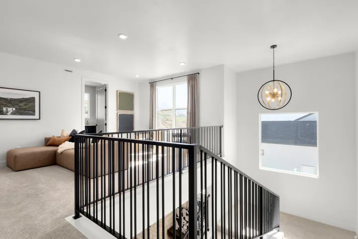 Corridor featuring light carpet, hanging lights, and an upstairs landing
