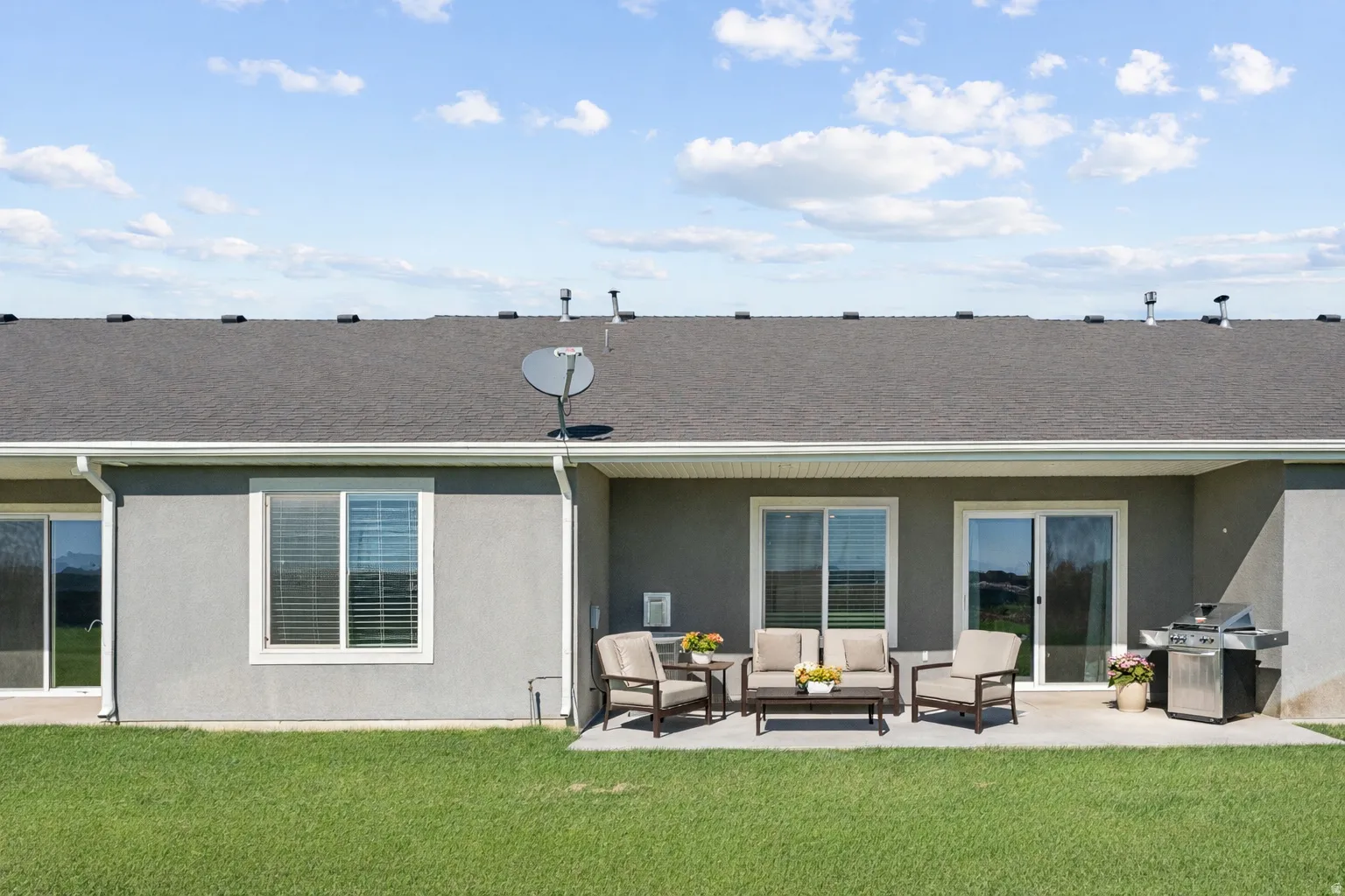 Back of property with stucco siding, a yard, a patio area, outdoor furniture, and roof with shingles