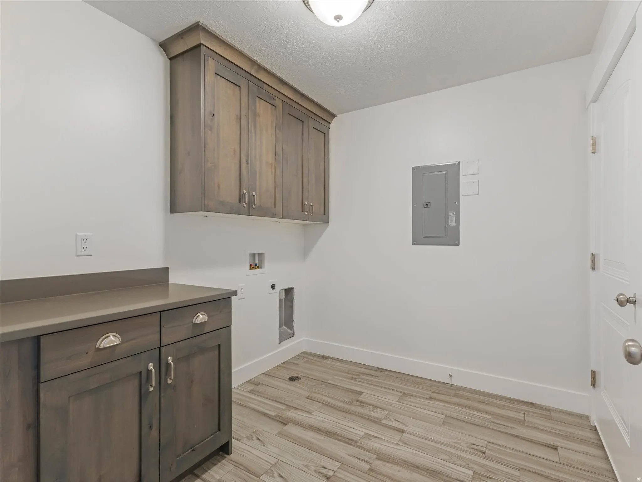 Laundry area with cabinet space, electric panel, light wood-type flooring, a textured ceiling, and hookup for a washing machine