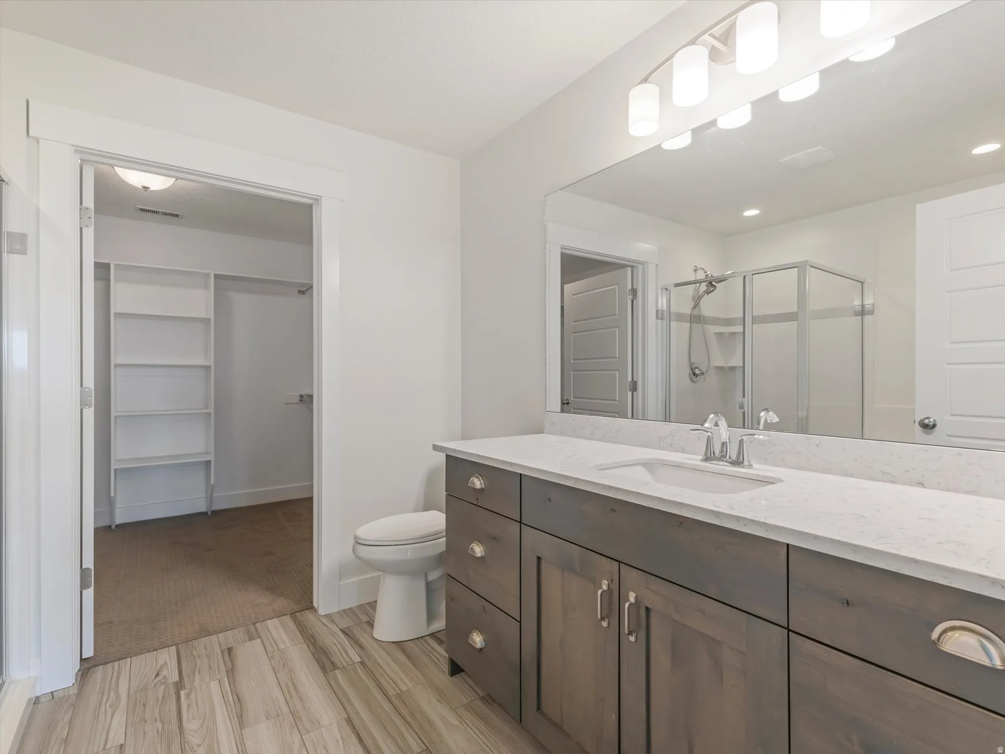 Bathroom with a spacious closet, a shower stall, vanity, and light wood-style flooring