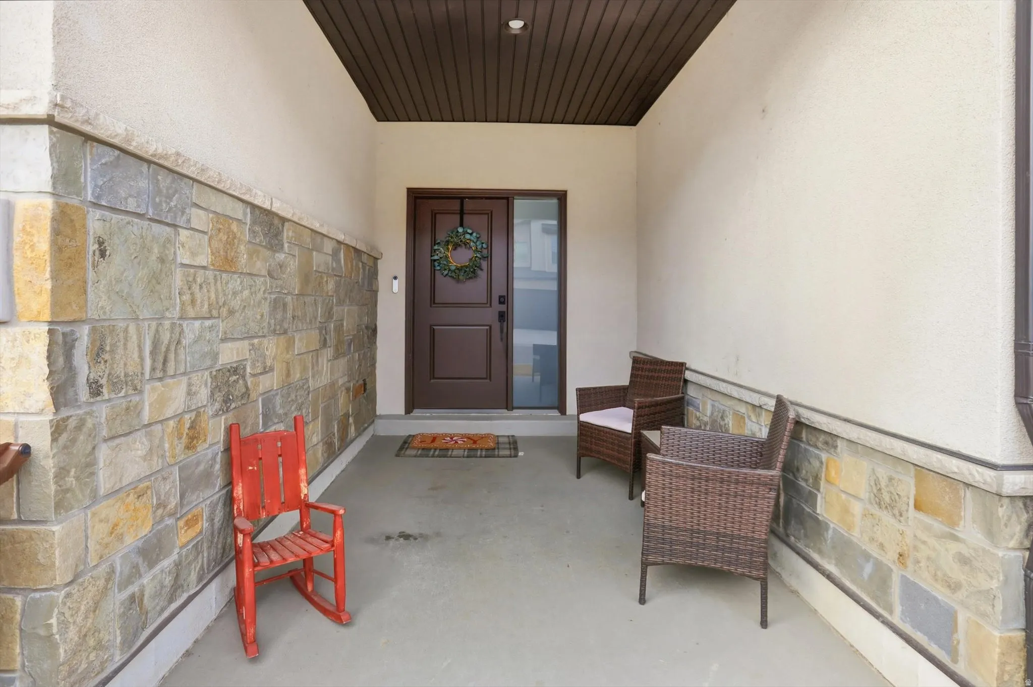 Property entrance with stucco siding, stone siding, and a patio area