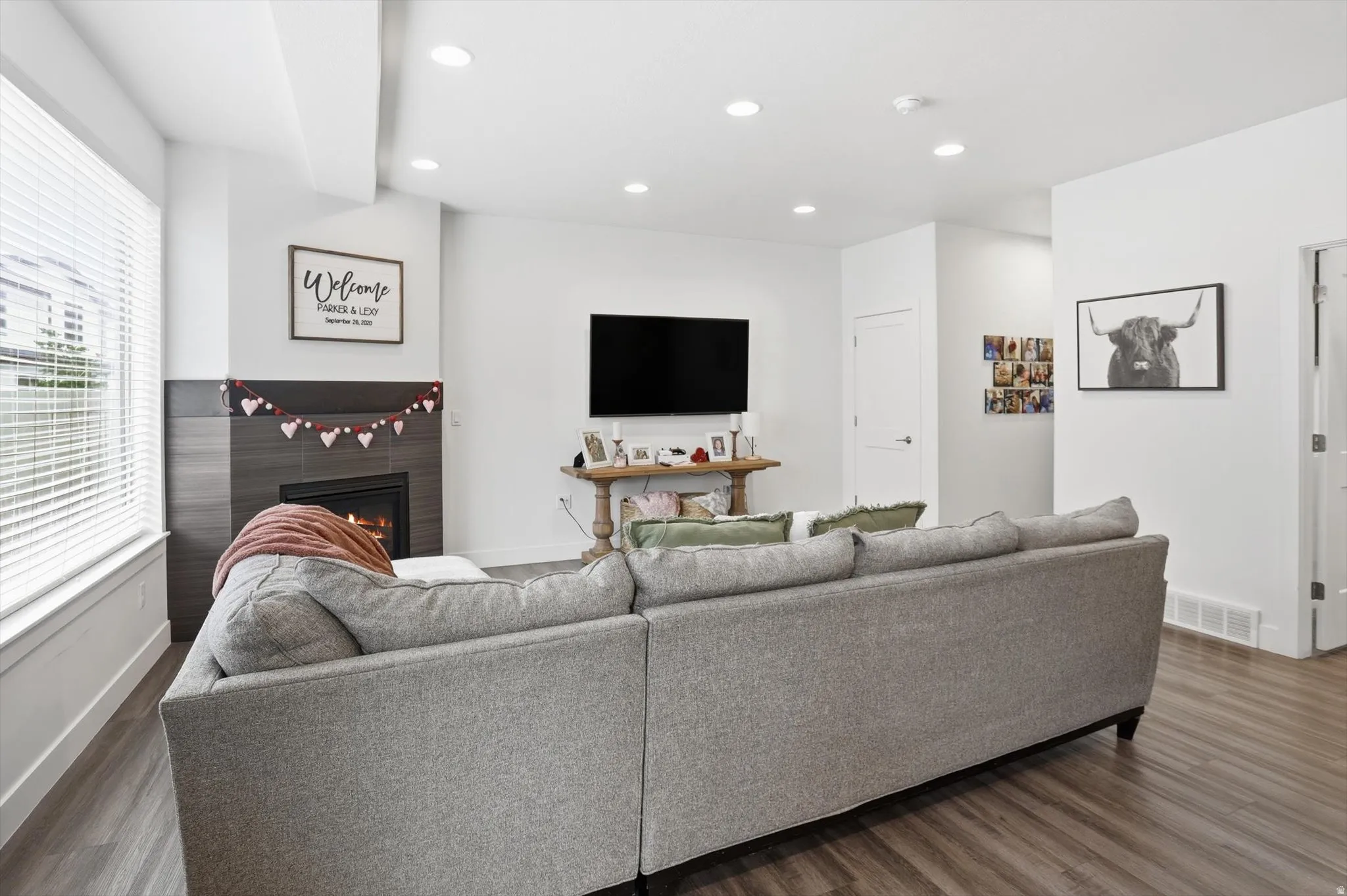 Living room with wood finished floors, a lit fireplace, and recessed lighting