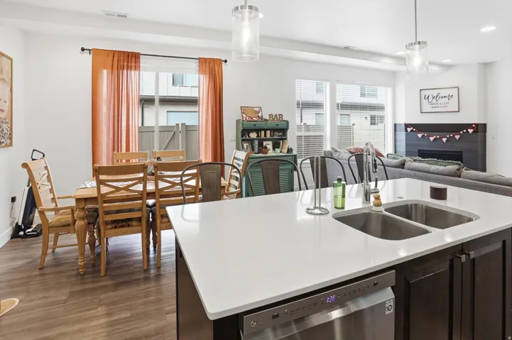 Kitchen with dark wood finish cabinetry, stainless steel dishwasher, dark wood finished floors, pendant lighting, and open floor plan