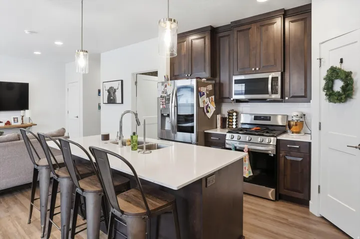 Kitchen featuring dark wood finish cabinetry, open floor plan, stainless steel appliances, a breakfast bar, and an island with sink