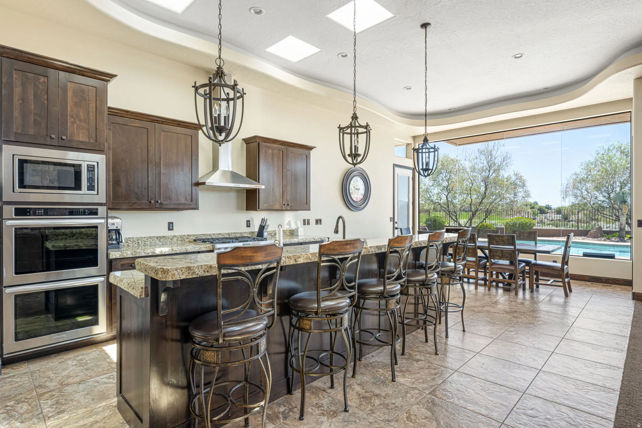 Kitchen with a tray ceiling, dark wood finish cabinets, a kitchen breakfast bar, a center island with sink, and stainless steel appliances