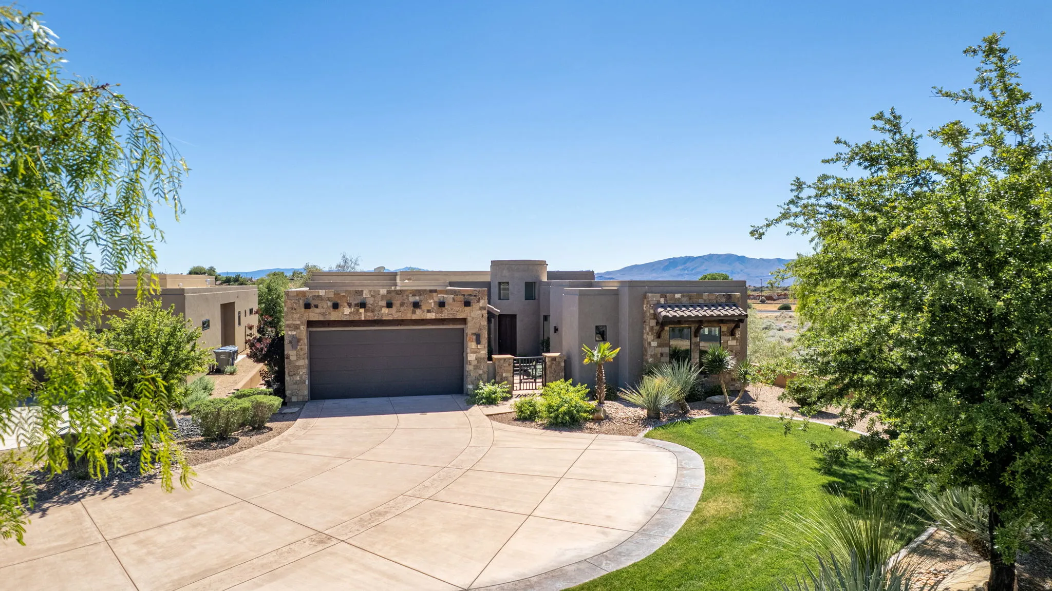 Pueblo revival-style home with concrete driveway, a mountain view, stucco siding, a garage, and a front lawn