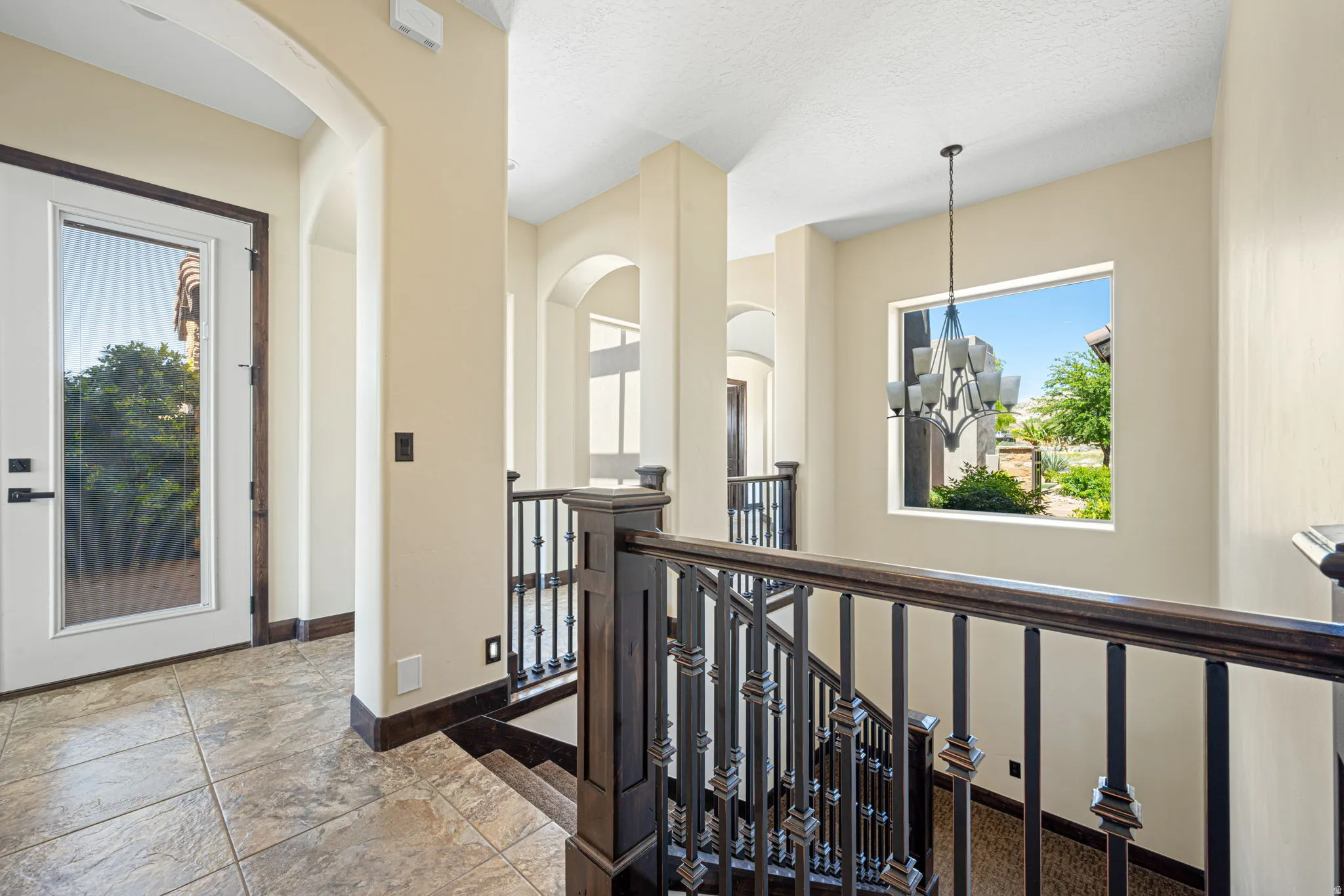 Corridor with an upstairs landing, stone tile flooring, suspended lighting, and a textured ceiling