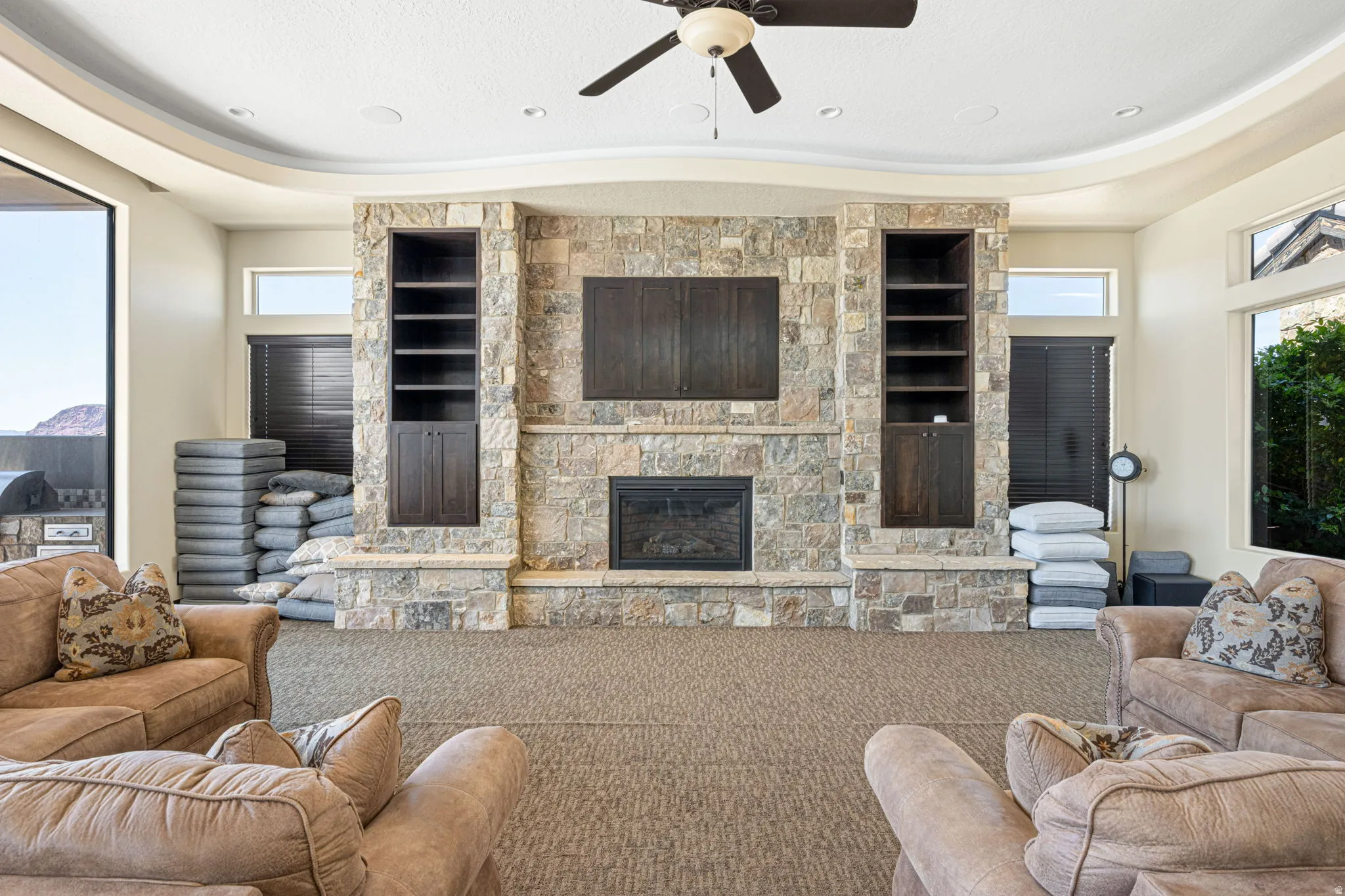 Carpeted living area with healthy amount of natural light, a ceiling fan, a tray ceiling, built in shelves, and a fireplace