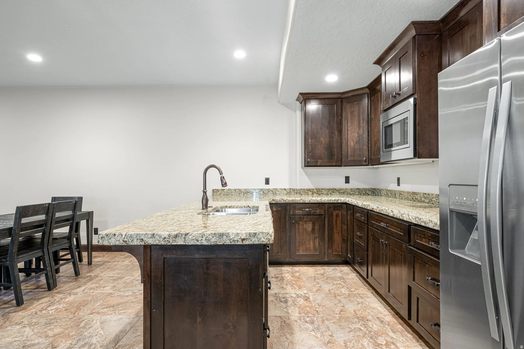 Kitchen with dark wood finish cabinets, a peninsula, stainless steel appliances, recessed lighting, and light stone finish floors