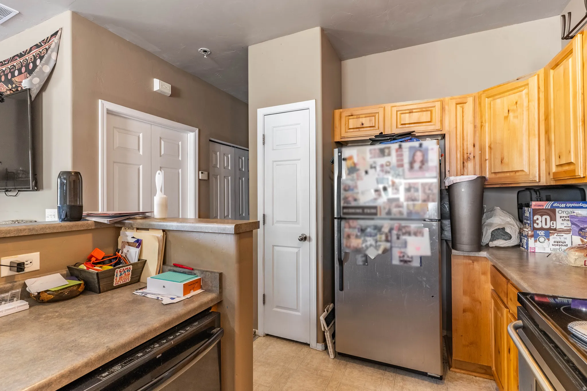 Kitchen featuring black appliances, light floors, light wood finish cabinetry, and light countertops