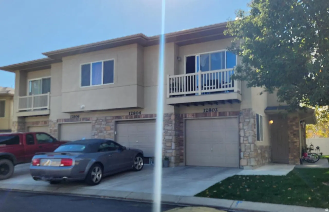 View of front of house with a balcony, stone siding, a garage, stucco siding, and driveway