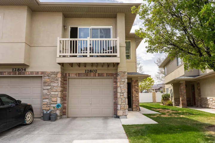 View of front of home with a balcony, an attached garage, stucco siding, stone siding, and driveway