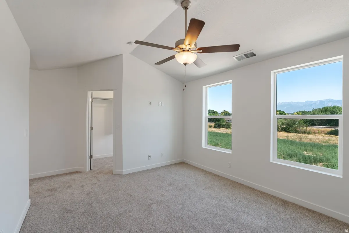 Unfurnished room featuring light colored carpet, lofted ceiling, and ceiling fan