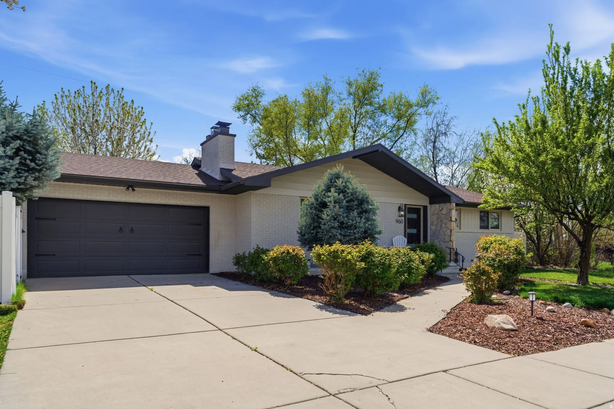 Ranch-style home featuring an attached garage, concrete driveway, a chimney, brick siding, and roof with shingles