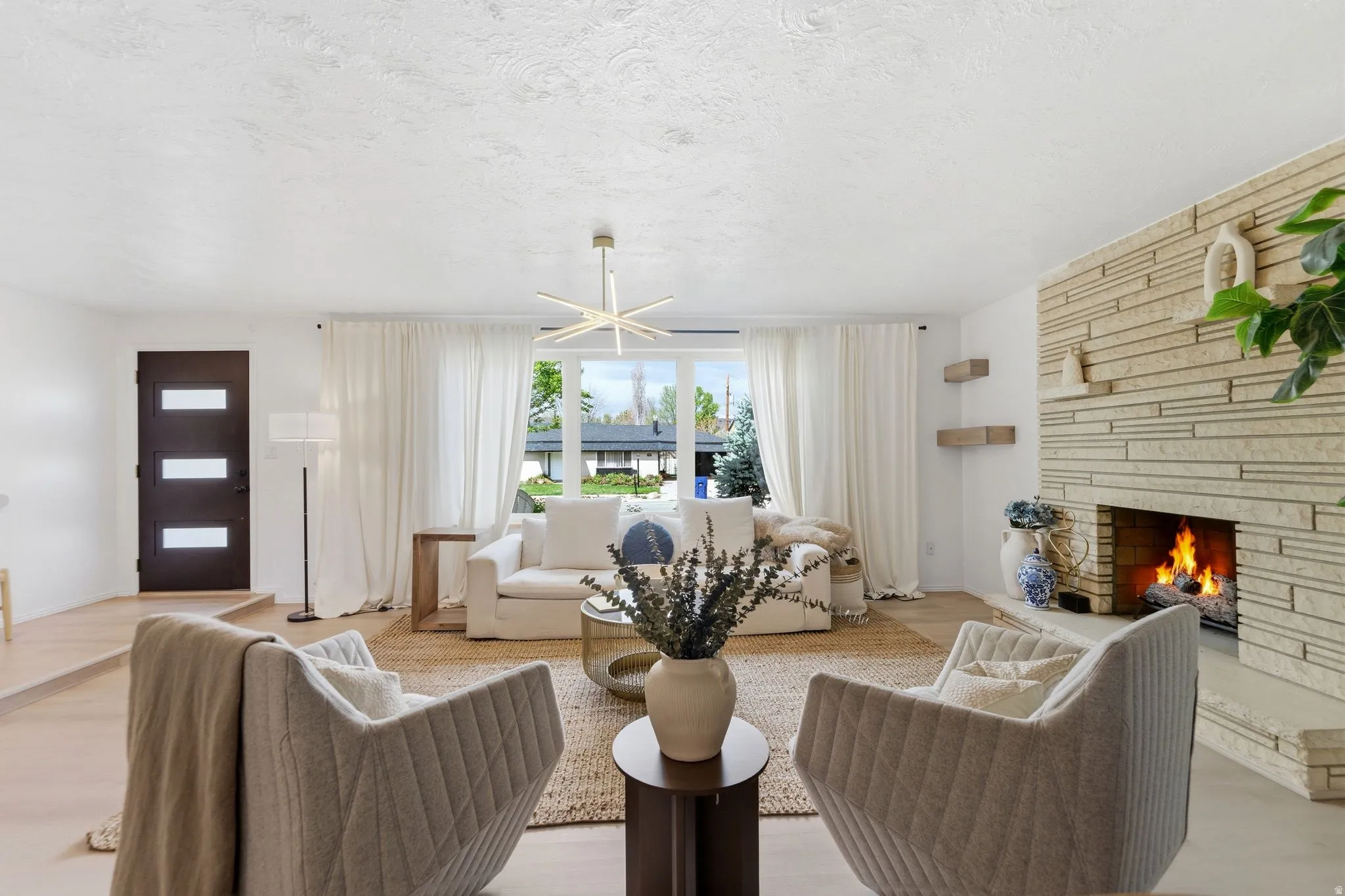 Living area with a fireplace, light wood finished floors, a textured ceiling, and a chandelier
