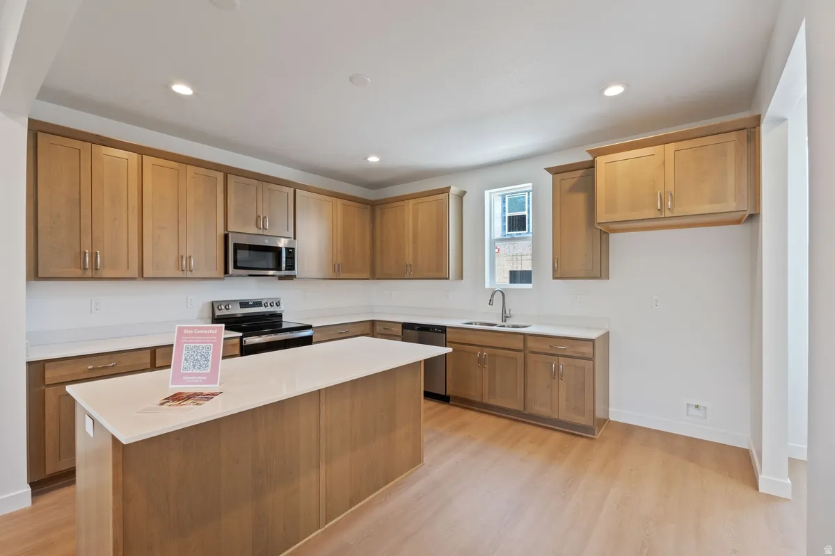 Kitchen with stainless steel appliances, wood finish cabinets, a kitchen island, light wood-type flooring, and recessed lighting