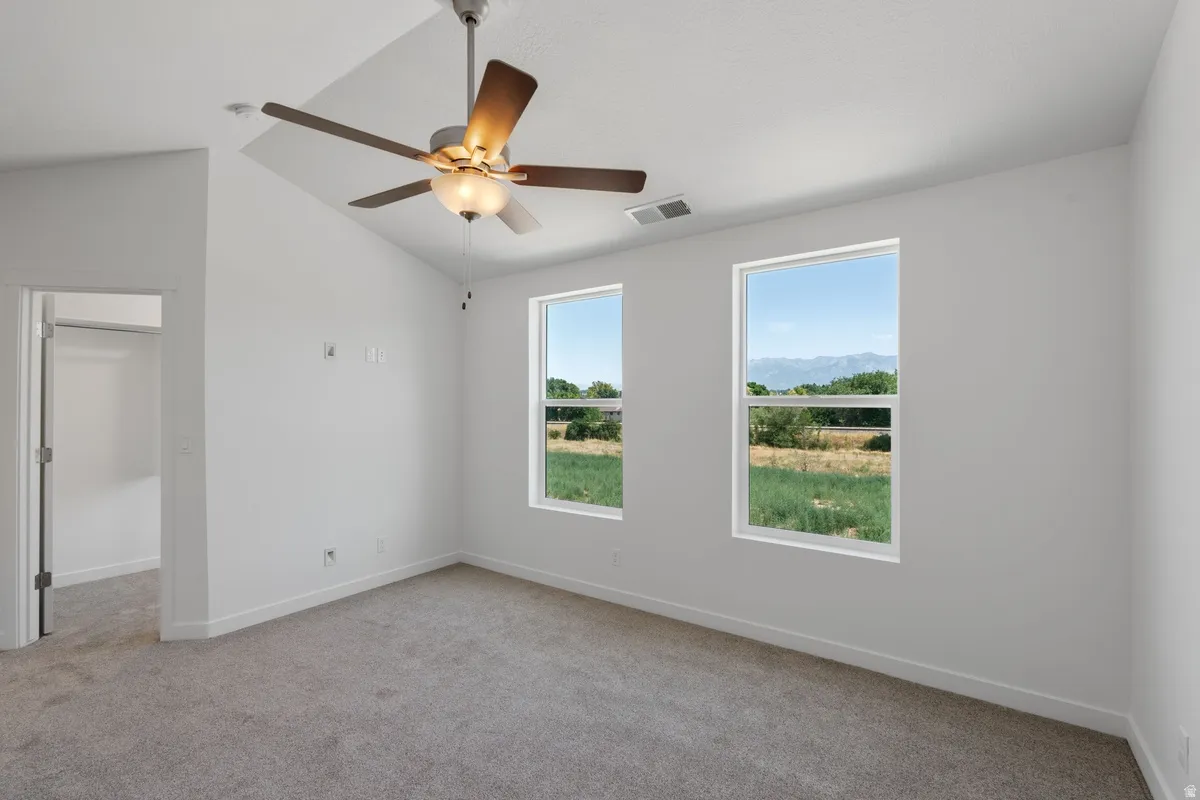 Unfurnished room featuring light carpet, ceiling fan, and vaulted ceiling