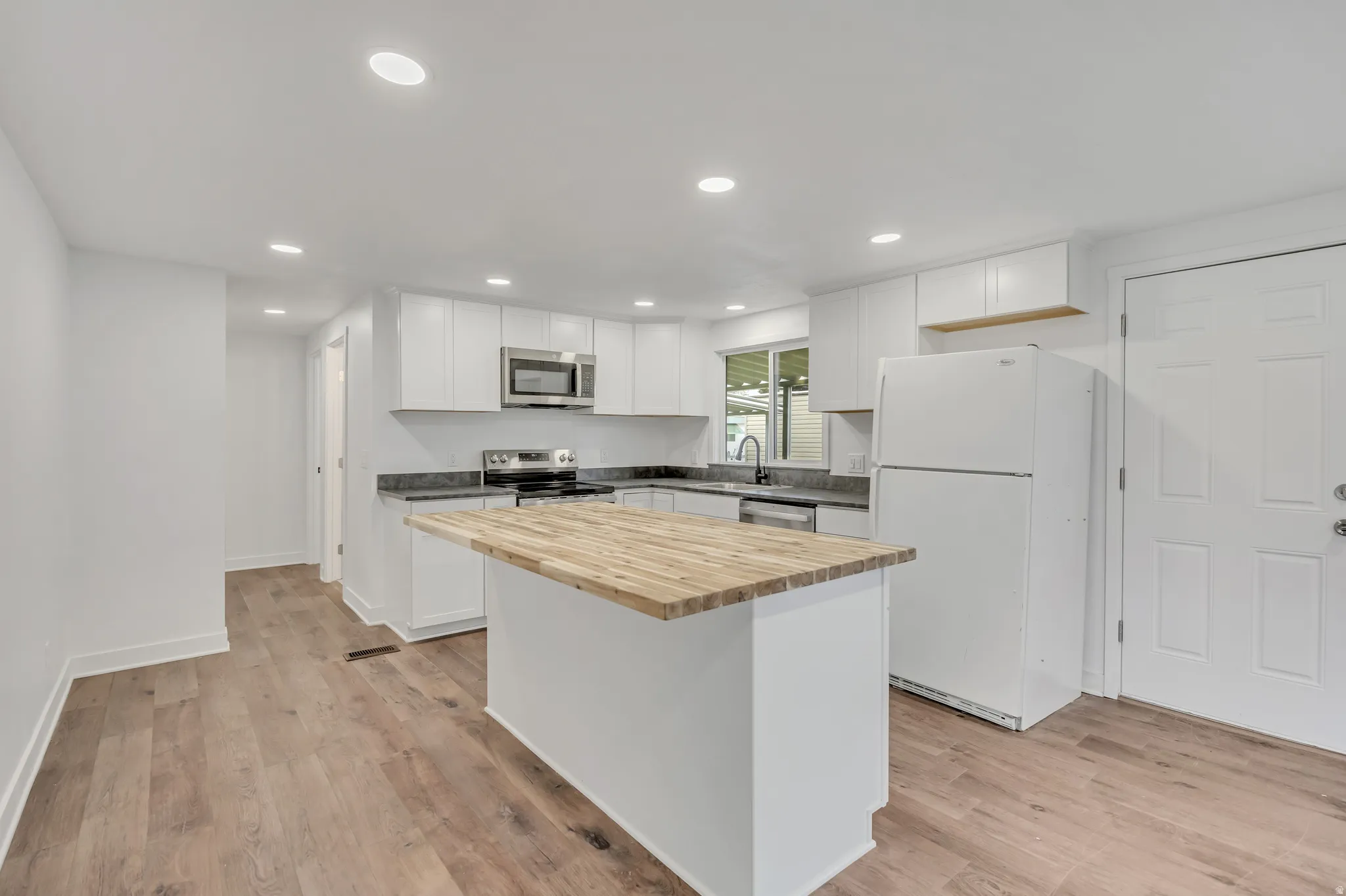 Kitchen featuring stainless steel appliances, butcher block countertops, white cabinetry, recessed lighting, and light wood-style floors