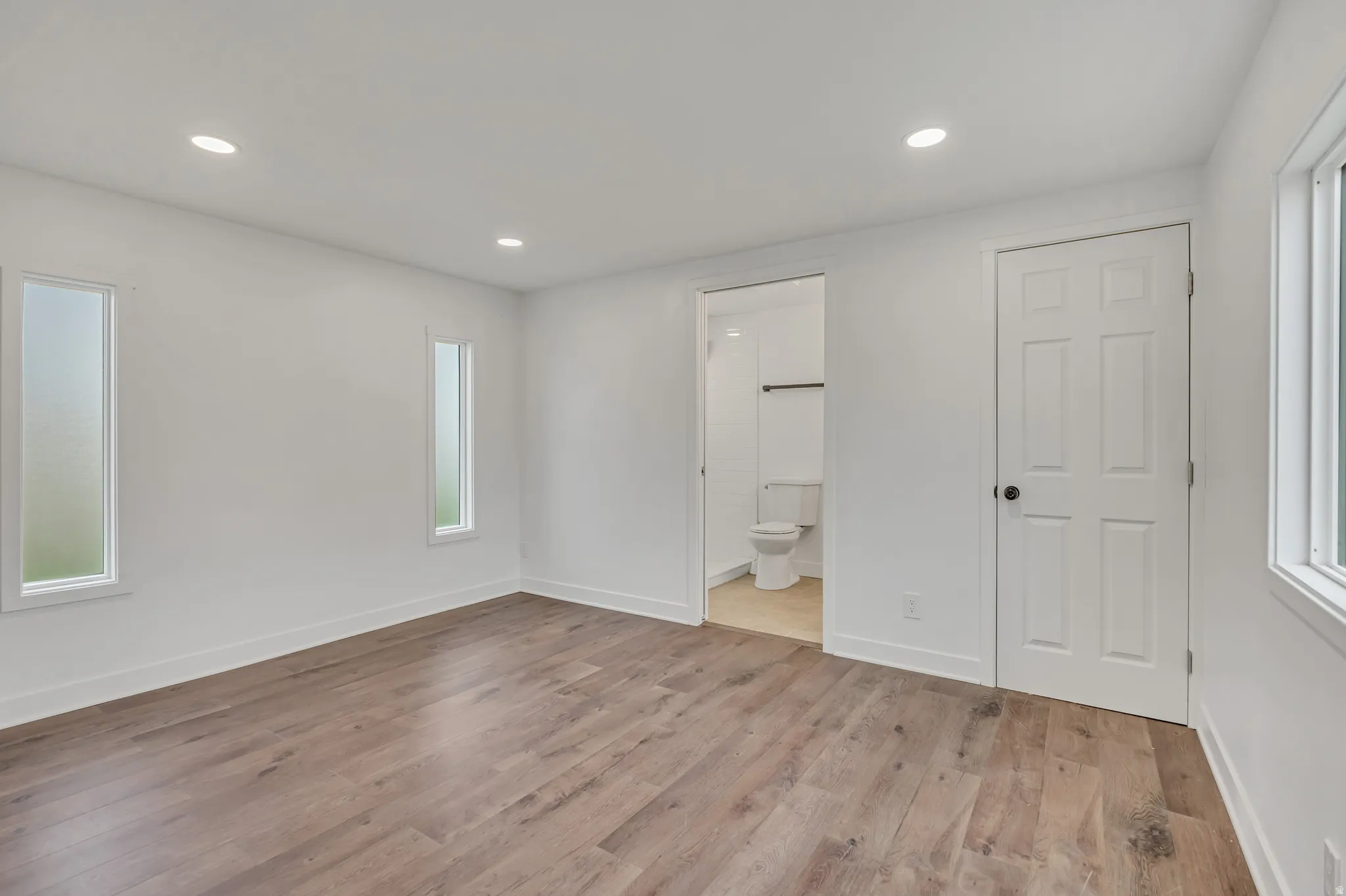 Unfurnished bedroom with recessed lighting, light wood-style flooring, multiple windows, and ensuite bathroom