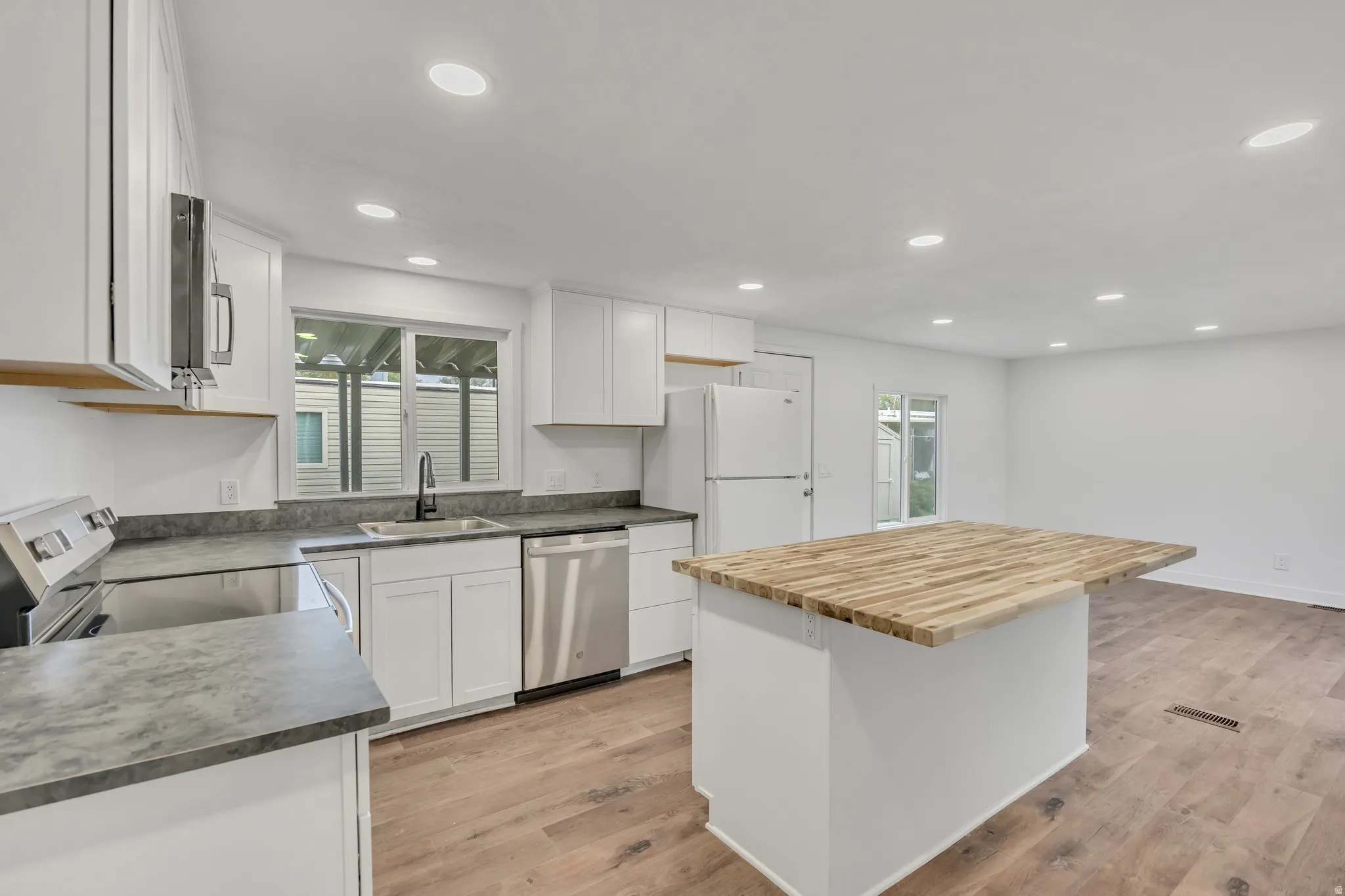 Kitchen with white cabinets, stainless steel appliances, butcher block countertops, light wood-style flooring, and a kitchen island
