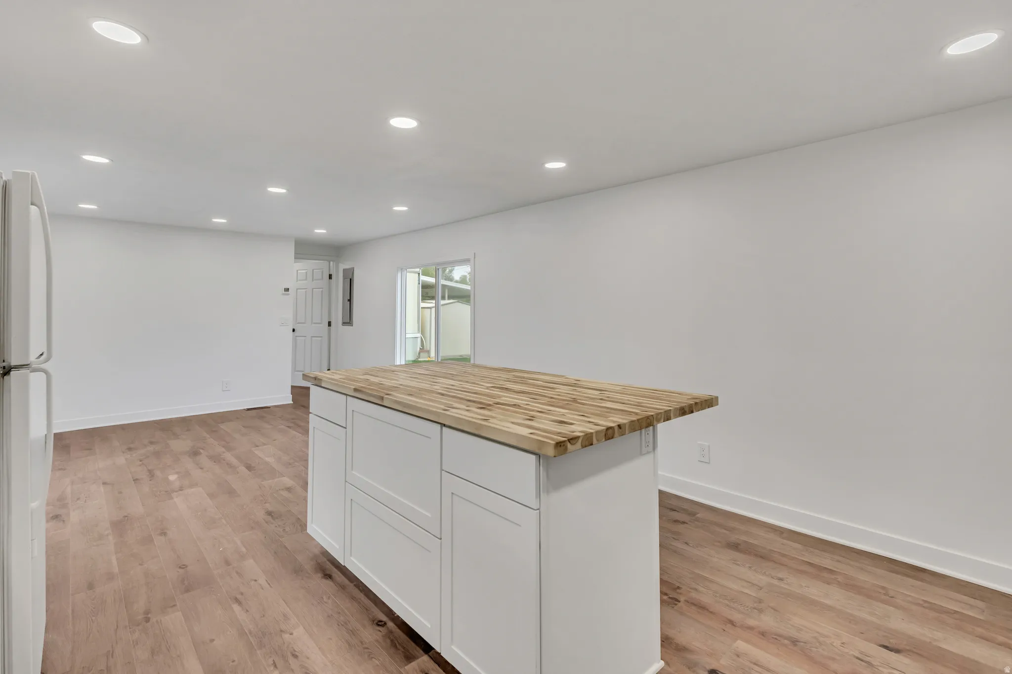 Kitchen with butcher block counters, recessed lighting, freestanding refrigerator, white cabinetry, and a kitchen island