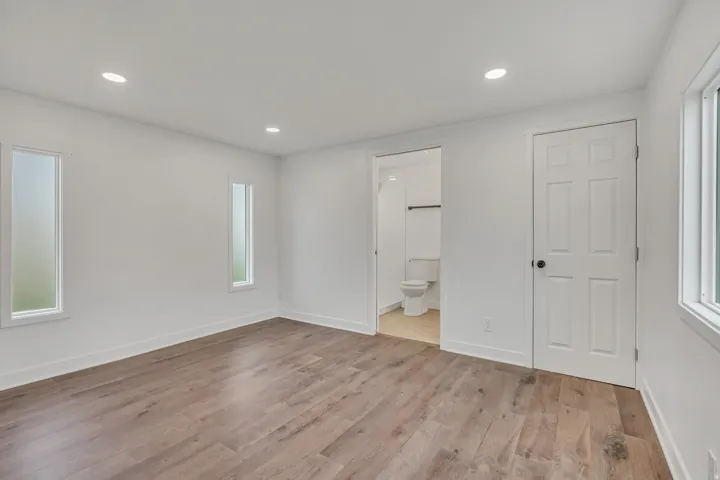 Unfurnished bedroom with recessed lighting, light wood-style flooring, multiple windows, and ensuite bathroom
