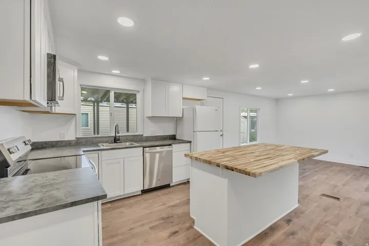 Kitchen with white cabinets, stainless steel appliances, butcher block countertops, light wood-style flooring, and a kitchen island