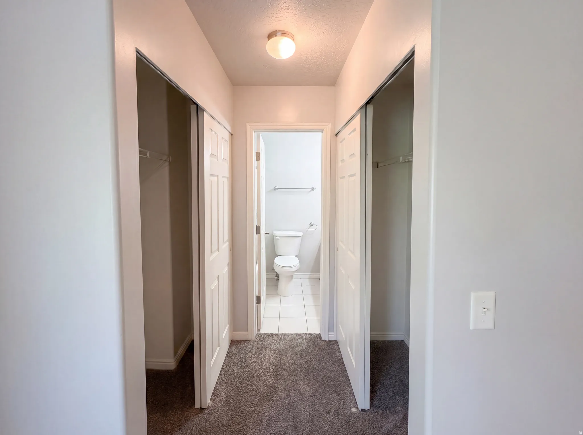 Hallway featuring dark carpet and a textured ceiling