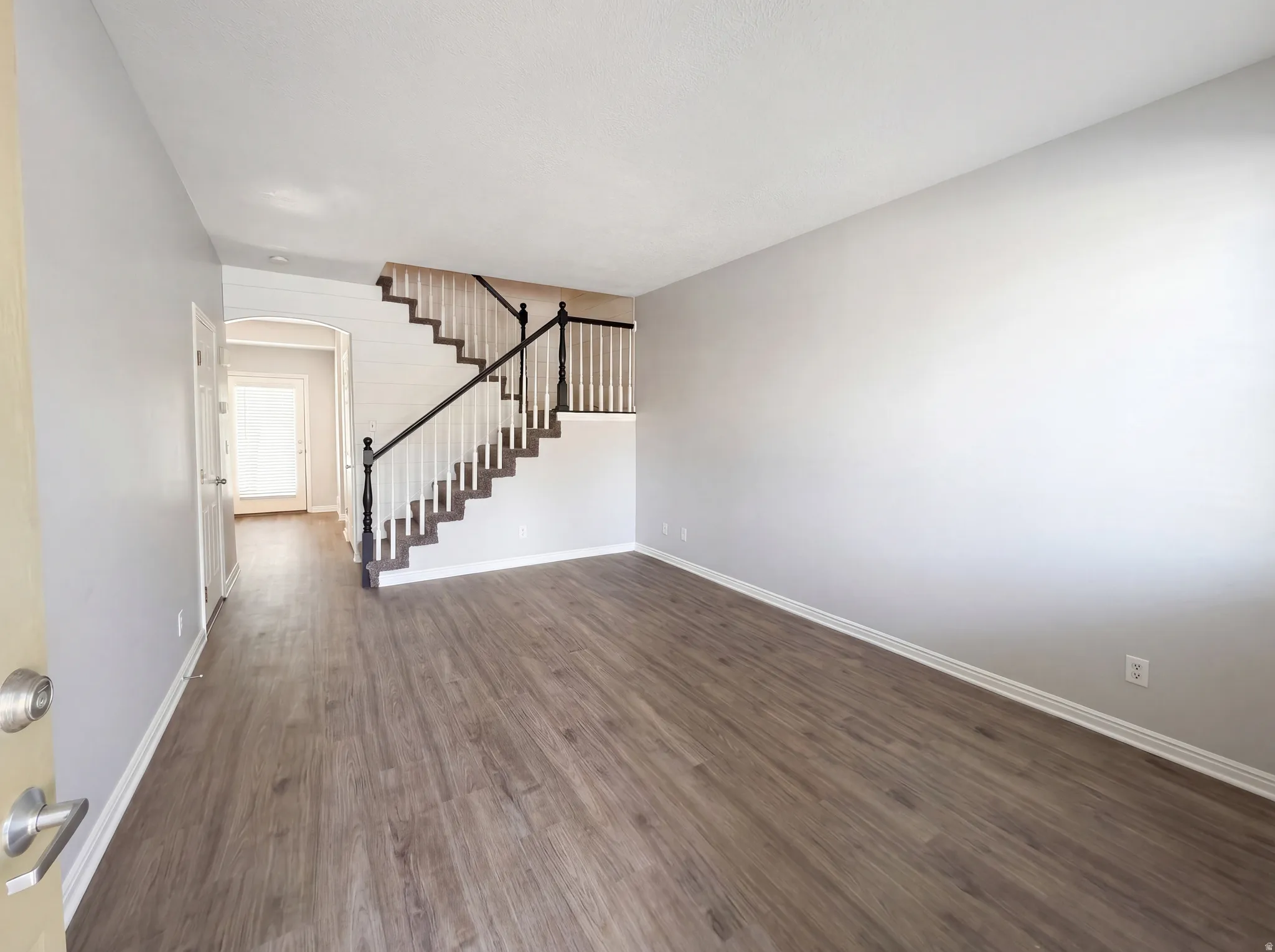 Unfurnished living room featuring arched walkways and dark wood-style flooring