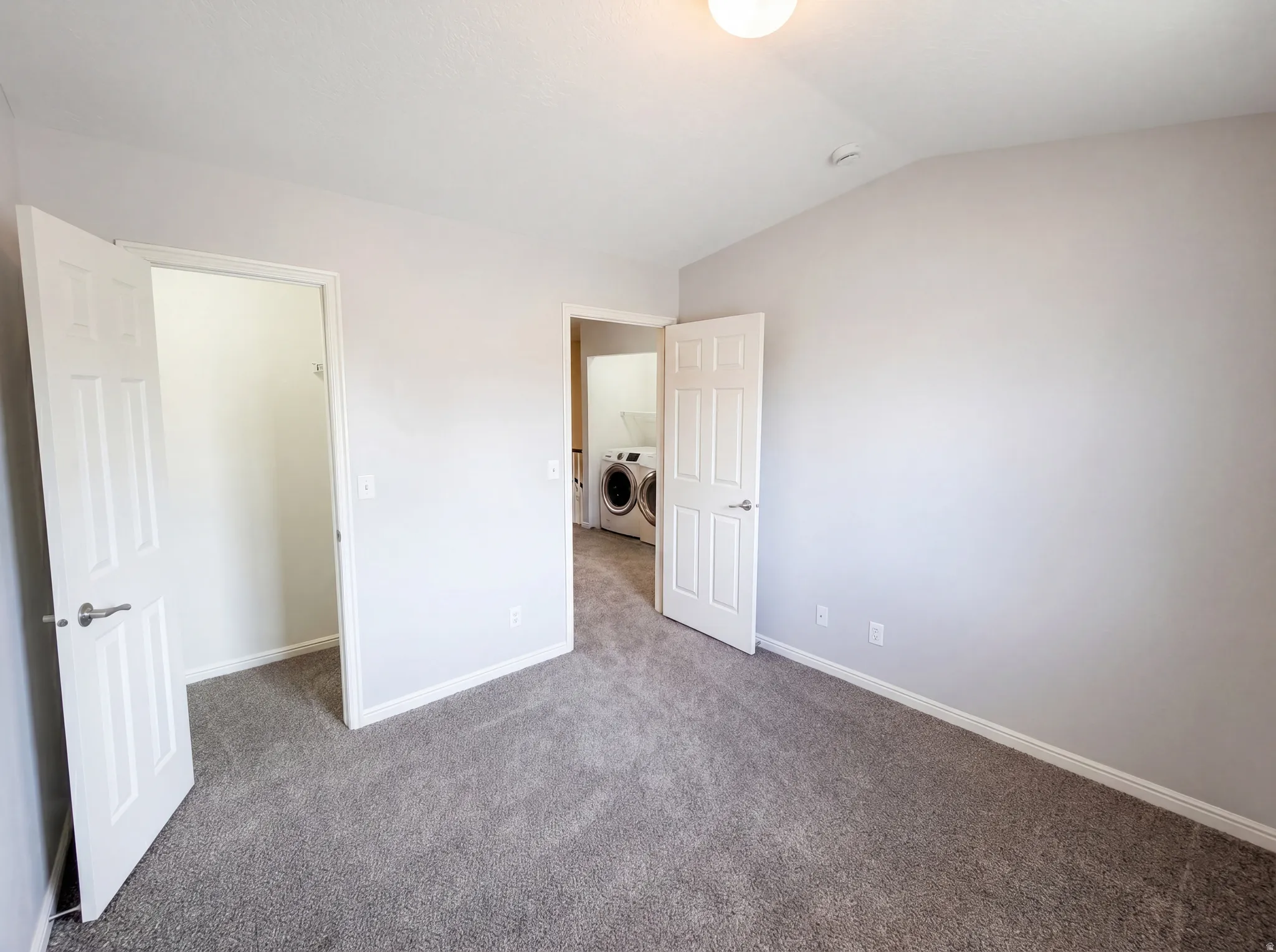 Unfurnished bedroom with carpet, vaulted ceiling, independent washer and dryer, and a walk in closet