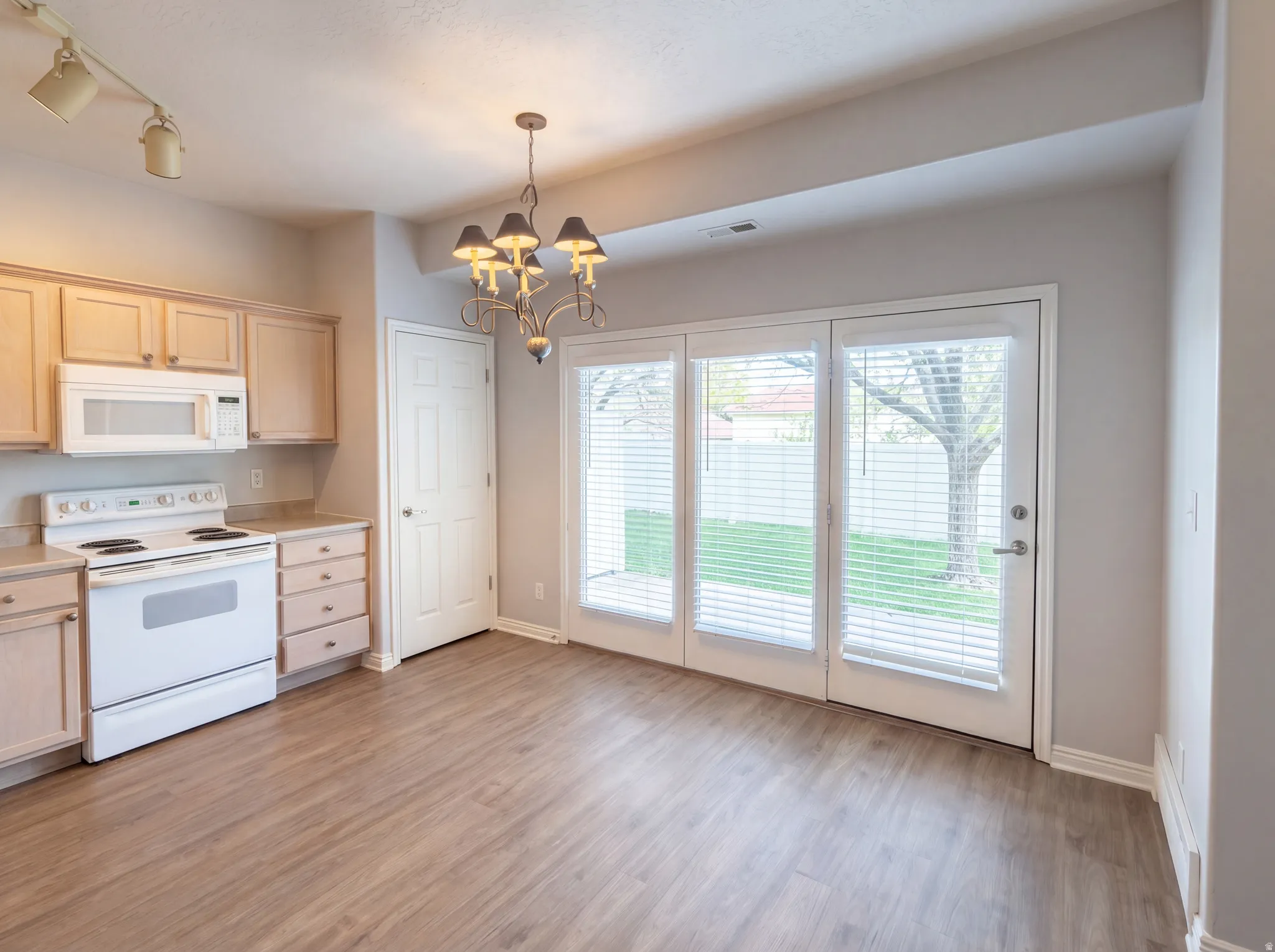 Kitchen featuring white appliances, light countertops, a chandelier, light wood-type flooring, and light wood finish cabinets