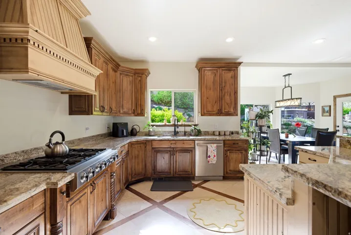 Kitchen featuring inlaid floor details, stainless steel appliances, pendant lighting, wood finish cabinetry, and light stone counters